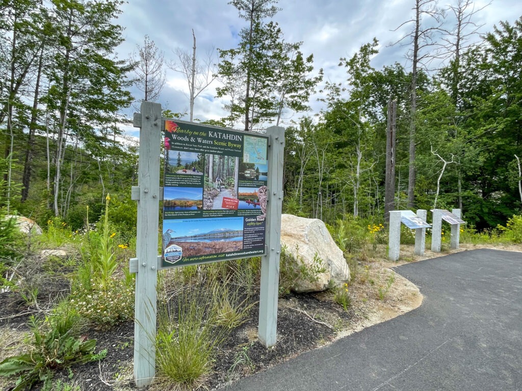 A Wooden Trail Sign Surrounded by Trees and Rocks, Indicating the Path Through the Forest.